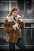 magnifique souriant fille dans élégant vêtements posant sur moderne balcon avec incroyable vue sur ville .portrait de une élégant à la mode blond adolescent avec fourrure manteau avec grand colliers portant dans balcon photo