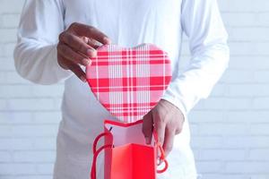 jeune homme, mettre un cadeau en forme de coeur dans un sac cadeau photo
