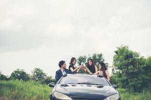 Heureux amis adolescents s'amusant assis sur la voiture le long de la route de campagne photo