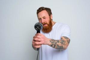 sérieux homme avec barbe jouer avec cheveux séchoirs une pistolet photo