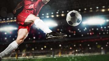 proche en haut de une football scène à nuit rencontre avec joueur dans une rouge uniforme coups de pied le Balle avec Puissance photo