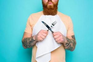 homme avec tatouages est prêt à manger avec coutellerie dans main photo