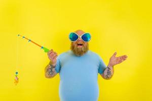 graisse homme avec barbe et des lunettes de soleil avoir amusement avec le pêche barre photo