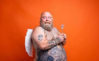 graisse étonné homme avec barbe , tatouages et ailes actes comme un la magie Fée photo