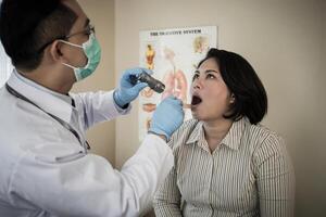 médecin dans blanc uniforme robe vérification les patients bouche avec lampe de poche photo