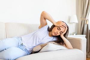 portrait d'une jolie femme assise sur un canapé à la maison avec un mal de tête, ressentant de la douleur et avec une expression de malaise. femme déprimée bouleversée allongée sur le canapé se sentant forte migraine migraine. photo