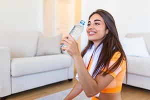 Jeune adulte femme en buvant l'eau de Plastique bouteille, séance sur aptitude tapis et repos après formation à Accueil photo