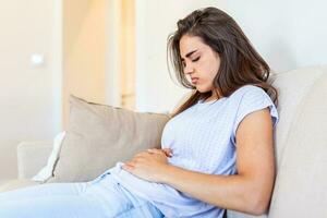 femme allongée sur un canapé qui a l'air malade dans le salon. belle jeune femme allongée sur le lit et se tenant la main sur le ventre. femme ayant des maux d'estomac douloureux au lit, période menstruelle photo