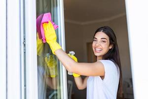 travaux ménagers et Entretien ménager concept - content femme dans gants nettoyage fenêtre avec chiffon et nettoyant vaporisateur à Accueil photo