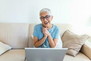 content sourire. personnes âgées femme sentiment content tandis que ayant vidéo appel. Sénior femme séance sur le canapé et ayant vidéo appel photo