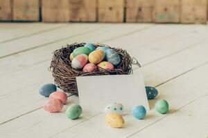 coloré Pâques des œufs dans le nid et papier carte sur bois table Contexte. photo