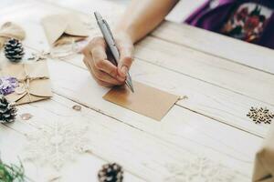 proche en haut de mains femme l'écriture vide liste de souhaits et Noël carte sur en bois table avec Noël décoration. photo