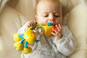 une petit enfant mensonges et pièces avec une jouet. bébé avec une jouet dans le sien bouche photo