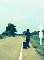 femme avec bagages faisant de l'auto-stop le long d'une route photo