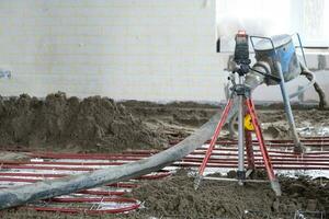 à moitié sec sol chape - une ouvrier pelles une construction mélange par une spécial manche pour cimentation et nivellement sur sous-sol chauffage tuyaux. photo