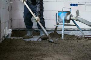 à moitié sec sol chape - une ouvrier pelles une construction mélange par une spécial manche pour cimentation et nivellement sur sous-sol chauffage tuyaux. photo