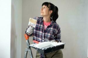 perplexe femme dans peindre rouleau et blanc peindre pour des murs dans mains fermer portrait. construction travail et cosmétique réparations dans loger, mur peinture, teinter, finition travail avec votre posséder mains photo