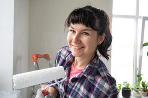 content femme dans peindre rouleau et blanc peindre pour des murs dans mains fermer portrait. construction travail et cosmétique réparations dans loger, mur peinture, teinter, finition travail avec votre posséder mains photo