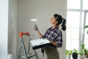 perplexe femme dans peindre rouleau et blanc peindre pour des murs dans mains fermer portrait. construction travail et cosmétique réparations dans loger, mur peinture, teinter, finition travail avec votre posséder mains photo