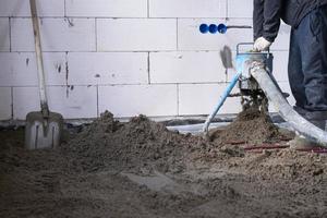 à moitié sec sol chape - une ouvrier pelles une construction mélange par une spécial manche pour cimentation et nivellement sur sous-sol chauffage tuyaux. photo