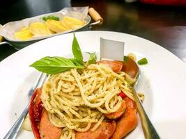 saucisse spaghetti dans thaïlandais style sur blanc céramique assiette avec cuillère et fourchette et Ail pain dans aluminium assiette et en bois table dans le restaurant. photo