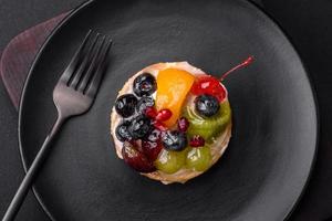 délicieux Frais Tarte avec myrtilles, cerises, les raisins sur une noir céramique assiette photo