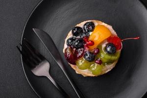 délicieux Frais Tarte avec myrtilles, cerises, les raisins sur une noir céramique assiette photo
