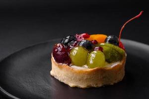 délicieux Frais Tarte avec myrtilles, cerises, les raisins sur une noir céramique assiette photo