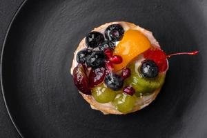 délicieux Frais Tarte avec myrtilles, cerises, les raisins sur une noir céramique assiette photo