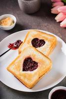 pain grillé avec une cœur rempli avec framboise confiture sur une plaque. petit déjeuner pour une couple. verticale vue photo