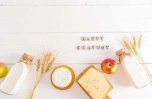 de fête Contexte pour le juif vacances de chavouot. laitier des produits, pomme, oreilles de blé sur une blanc Contexte avec une de félicitations texte. Haut voir. photo