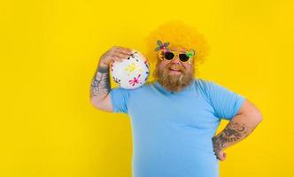 graisse homme avec perruque dans tête et des lunettes de soleil avoir amusement avec une Balle photo