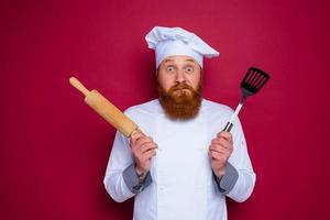 sceptique chef avec barbe et rouge tablier chef détient en bois roulant épingle photo