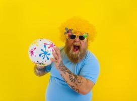 graisse homme avec perruque dans tête et des lunettes de soleil avoir amusement avec une Balle photo