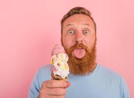 homme avec barbe et tatouages mange une gros crème glacée photo