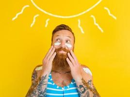 homme avec tatouages et maillot de bain met sur crème solaire photo