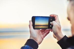 une homme prise une photo de le magnifique le coucher du soleil sur le sien téléphone