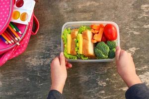 sandwichs, des fruits et des légumes dans nourriture boîte, sac à dos sur vieux en bois Contexte. concept de enfant en mangeant à école. Haut voir. plat poser. photo