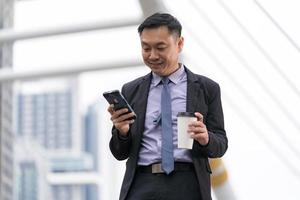 homme d & # 39; affaires asiatique debout et tenant un téléphone mobile avec des immeubles de bureaux dans le fond de la ville photo