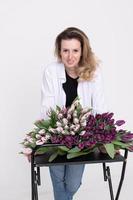 une charmant fille penché plus de une table avec différent variétés de tulipes. bouquet de violet tulipes photo