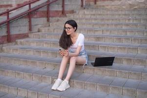 une fille avec des lunettes est séance sur le escaliers avec une portable sur sa tour photo