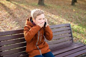 un émotif garçon pourparlers sur le téléphone couvertures le sien bouche avec le sien main et des rires photo