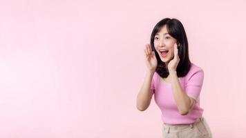 portrait magnifique Jeune asiatique femme expression jaune crier annoncer nouvelles de la communication message ou crier bruyant voix avec main à côté de bouche geste isolé sur rose pastel Contexte. photo