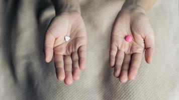 femelle mains tenir et offre deux choix médicament pilules capsule pour choisi. blanc et rose bonbons ou Médicaments comparer à choisir depuis. concept décision fabrication ou indécision. photo