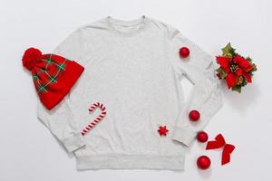 proche en haut gris Vide modèle sweat-shirt copie espace. Noël vacances concept. Haut vue maquette sweatshirt à capuche, chapeau. rouge vacances décorations sur blanc Contexte. content Nouveau année accessoires. Noël tenue photo