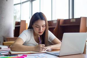 Jeune asiatique élèves dans décontractée porter faire devoirs et utilisation une La technologie portable dans le Université bibliothèque. le élèves sont recherche pour connaissance et sont en train de préparer pour le examen. photo