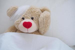 nounours ours avec une blessure robe, blessure et cassé mains. en train de dormir dans lit. maladie de les enfants photo