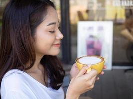 mignonne fille profiter en buvant café dans gratuit temps à l'intérieur le café magasin avec une détendu geste avec une sourire. photo