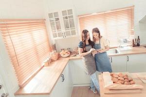 magnifique lesbienne couple cuisine en bonne santé nourriture, à la recherche sur numérique tablette à moderne cuisine intérieur. homosexuel rapports et en bonne santé en mangeant concept. lgbt, lgbtq Accueil en ligne cuisine. chaud Ton. photo