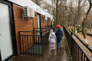 retour de frère avec sœur en marchant sur terrasse de un étage modulaire Maisons dans printemps pluvieux forêt. photo